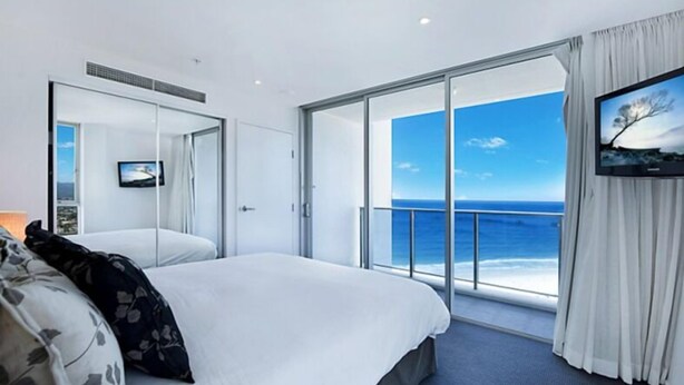 Una habitación de hotel moderna con una cama grande, televisión y un balcón con vista al océano.