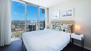 Un cuarto de hotel con una cama grande, dos mesitas de noche, vistas de la ciudad y un cuadro con un paisaje urbano en la pared.
