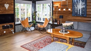 A cozy living room with a wooden floor, a red and white patterned rug, a wooden coffee table, two leather chairs, a grey sofa, and a large window with a view of trees. - Gorgeous home in Fyresdal (Fyresdal)