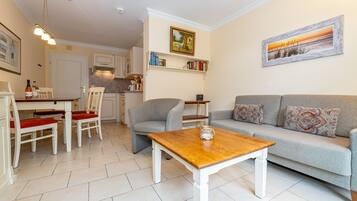 A modern living room with a grey sofa, a wooden coffee table, and a dining area with a white table and red chairs.