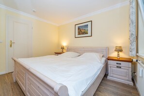 A bedroom with a large bed, two bedside tables with lamps, a door, and a framed picture on the wall.