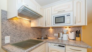 Una cucina compatta con mobili bianchi, un microonde Bosch, una macchina da caffè e una lavastoviglie.