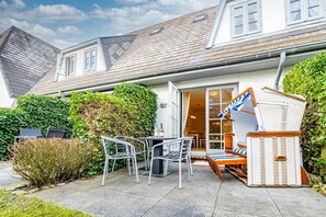 A house with a patio area featuring a table and chairs, a wicker chair, and a small wooden structure.