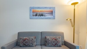 Un divano grigio con cuscini decorati, un quadro incorniciato raffigurante un tramonto e una lampada da terra.