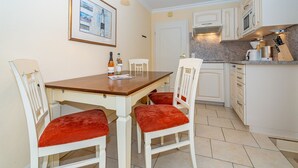 Una cucina compatta con mobili bianchi, un tavolo di legno e sedie rosse imbottite.