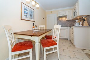 A compact kitchen with white cabinets, a wooden table, and red cushioned chairs.