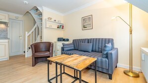 Ein gemütliches Wohnzimmer mit einer Couch, einem Holztisch, einem braunen Ledersessel, einem Bücherregal und einer Stehlampe.