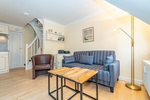 Un salón acogedor con un sofá, una mesa de centro de madera, un sillón de cuero marrón, una estantería y una lámpara de pie.