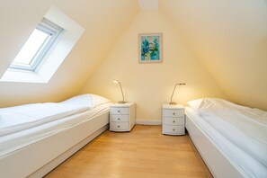 Una habitación pequeña y bien iluminada con dos camas individuales, suelo de madera, un tragaluz y un cuadro en la pared.