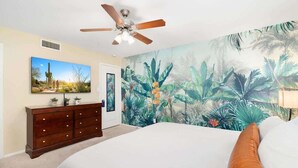 A bedroom with a bed, a ceiling fan, a dresser, a painting, and a tropical mural on the wall. - 4BR Scottsdale Tempe Oasis! Heated Pool & Hot Tub! (Tempe)