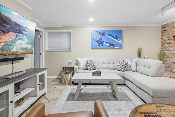 Una sala de estar moderna con un sofá modular, un televisor de pantalla plana y un cuadro grande de aviones.