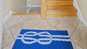 Una escalera con escalones de madera que sube a un piso superior, una alfombra azul con diseño blanco en la parte inferior y un soporte para tablas de surf fijado a la pared.