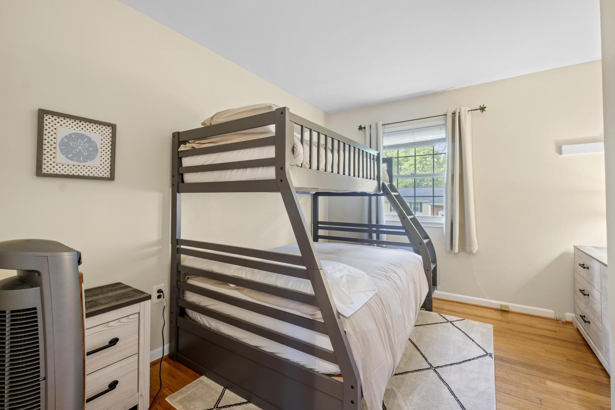 Une chambre avec un lit superposé, une fenêtre, un radiateur et une commode.
