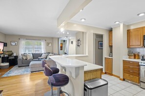 Una cocina moderna con armarios de madera, una isla integrada y un comedor con sofá gris y sillas moradas.