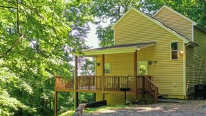 A yellow cabin with a porch, surrounded by trees.