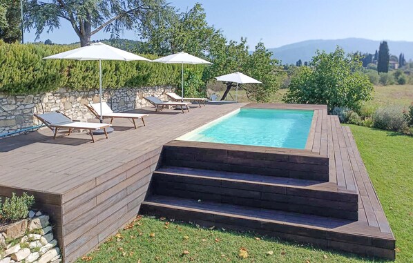 Una terraza de madera con piscina, sillas de descanso y sombrillas.