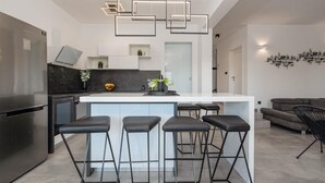 A modern kitchen with a central island, bar stools, a refrigerator, and a dining area with a sofa and chairs. - Luxurious home in Mandre (Mandre)