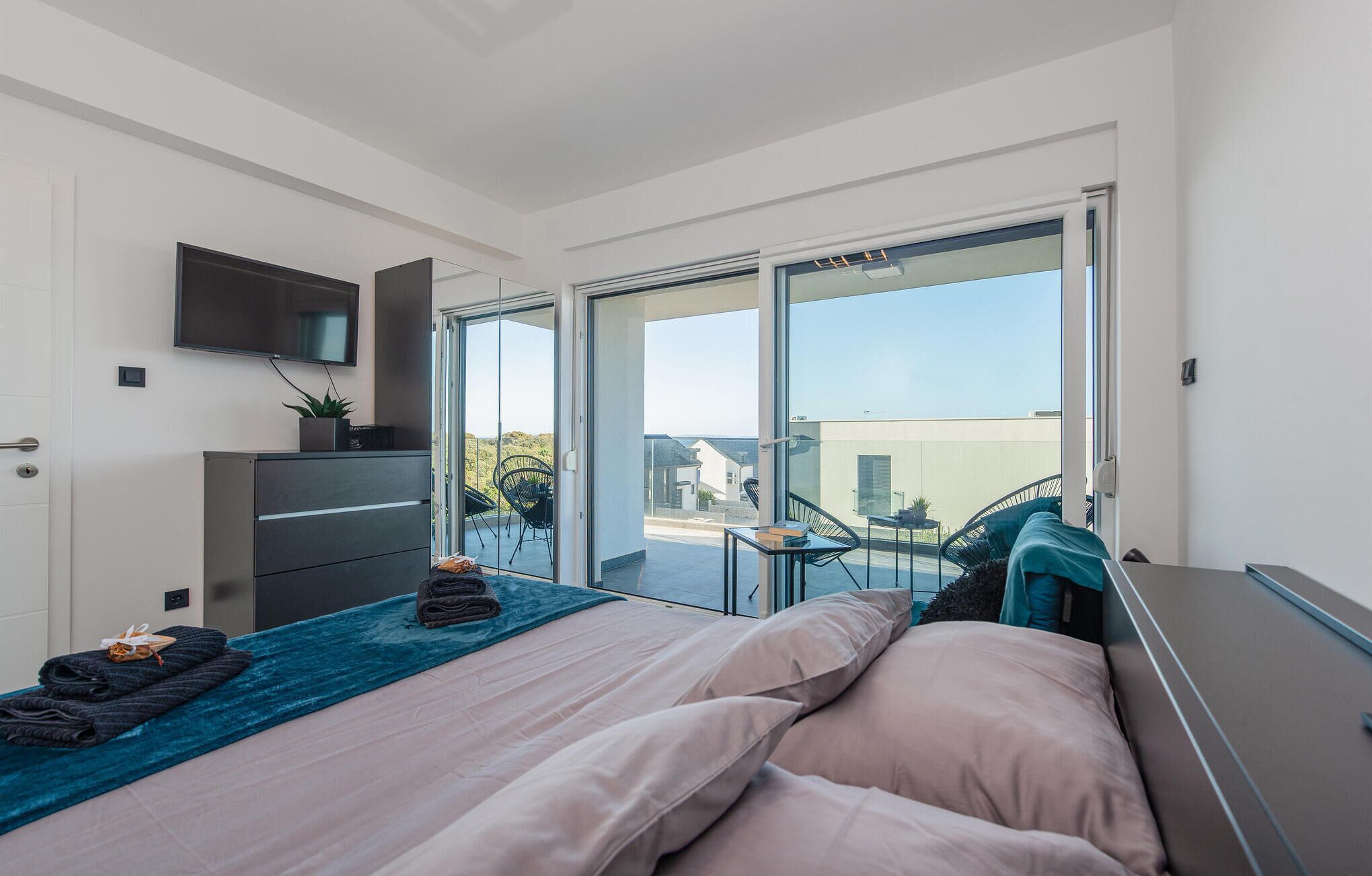 A modern bedroom with a bed, a desk, and a TV mounted on the wall.