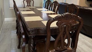 A dining area with a large wooden table and matching chairs, a sofa, a TV, and a clock on the wall.