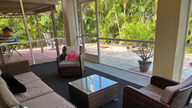 A covered outdoor seating area with wicker furniture and a glass coffee table.