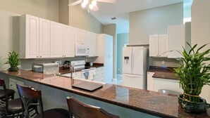 A modern kitchen with white cabinets, a granite countertop, a ceiling fan, and a refrigerator.