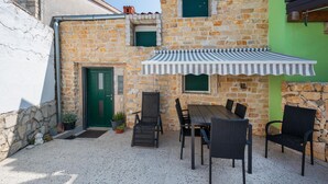 Un bâtiment en pierre avec une porte verte, des sièges en plein air avec des chaises et une table, et un auvent à rayures.