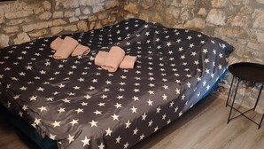 Un lit recouvert d’une couverture à motifs étoilés, deux serviettes enroulées et une petite table ronde.