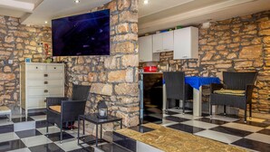 Une pièce avec un mur en pierre, un téléviseur à écran plat, une kitchenette et un sol à carreaux noirs et blancs.