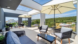 A modern outdoor patio with wicker furniture, large umbrellas, and a view of the countryside. - Lovely apartment in Sukosan (Sukosan)