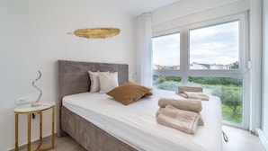 A modern bedroom with a large bed, a bedside table, and a view of the outdoors. - Lovely apartment in Sukosan (Sukosan)
