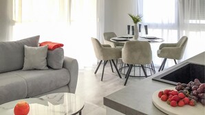A modern living room with a grey sofa, a round glass coffee table, and a dining area with a round table and chairs. - Lovely apartment in Sukosan (Sukosan)