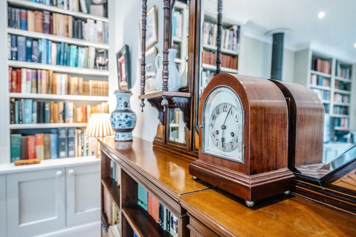 A wooden bookshelf with books, a blue and white vase, and a wooden clock.