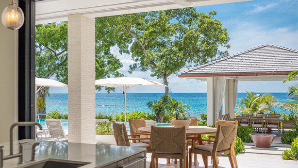 A modern kitchen with a view of the ocean, outdoor seating with umbrellas, and a patio area with a view of the sea.