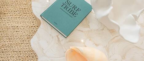 Een boek met de titel 'SURF TRIBE' op een structuurrijk oppervlak, met een geweven mat en een wit, organisch vormig object.