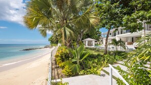 A beachfront property with a pool, palm trees, and a white building with a covered patio.