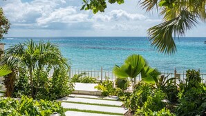A pathway leading to a beach with a clear view of the ocean, surrounded by lush greenery and a metal railing.