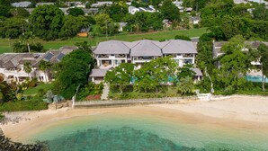 An aerial view of a coastal property with a beachfront and a large house with multiple levels and a covered patio.