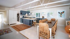 Una cocina moderna con una isla central, comedor con sillas de mimbre y un amplio ventanal que proporciona luz natural.