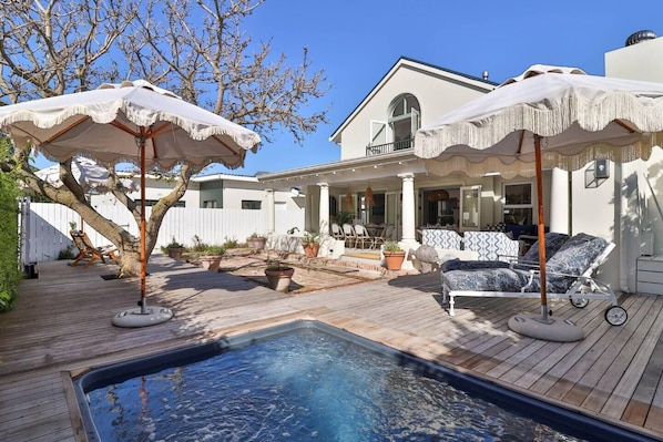 A pool with a wooden deck, outdoor furniture, and umbrellas.