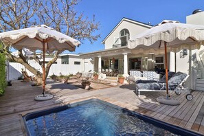 A pool with a wooden deck, outdoor furniture, and umbrellas.