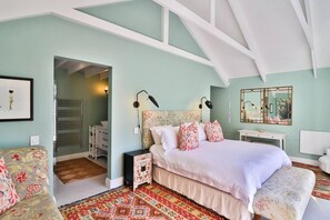 A bedroom with a large bed, a nightstand, a dresser, a chair, and a mirror.