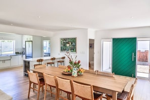 A modern kitchen with white cabinets, a large island, and a dining area with a wooden table and wicker chairs. - Zo'luha | Spacious family home | Mountain View (Hermanus)
