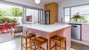 A modern kitchen with a large island, wooden stools, and a view of the outdoors.