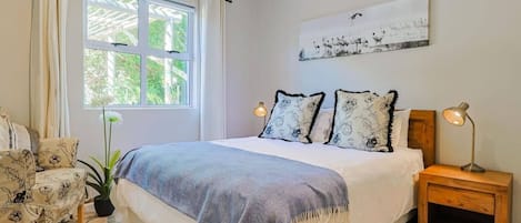 A bedroom with a bed, a nightstand, a chair, a window, and a painting on the wall.