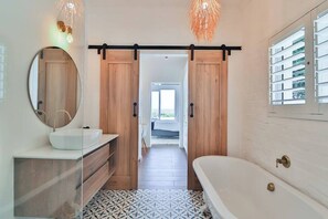 Une salle de bain moderne avec une baignoire sur pieds, un miroir rond et un meuble-lavabo en bois.
