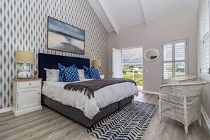 A bedroom with a bed, a nightstand, a lamp, a window with a view, a chair, and a patterned rug.