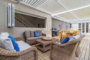 An outdoor covered patio with wicker furniture, a grill, and a staircase leading to an upper level.