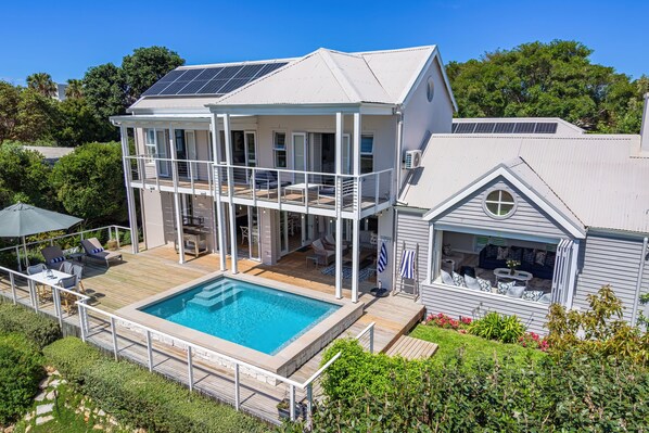 A two-story house with a swimming pool, solar panels, and a covered outdoor seating area.