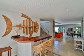 Ampla sala de estar com uma escultura de peixe em madeira, uma escada e uma mesa de bilhar.