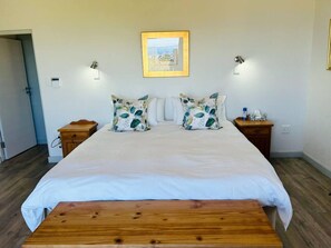 A bedroom with a bed, two nightstands, a wooden bench, a framed picture on the wall, and a door.